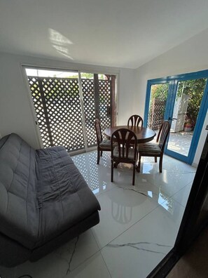 Una habitación con sofá, una mesa de comedor con sillas y un ventanal corredero que da a un espacio exterior.