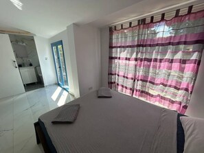 Un dormitorio con cama, una ventana con cortinas a rayas y un baño visible a través de una puerta abierta.