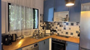 A compact kitchen with blue cabinets, a stainless steel refrigerator, a built-in oven, a washing machine, and a coffee maker. - Newly Renovated Apt with Private Garden - 7 Min Walk to Beach (Paphos)
