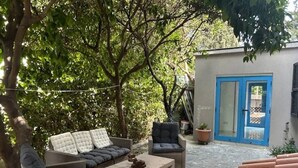 An outdoor patio area with a sofa, armchair, and coffee table, surrounded by trees and a blue door. - Newly Renovated Apt with Private Garden - 7 Min Walk to Beach (Paphos)