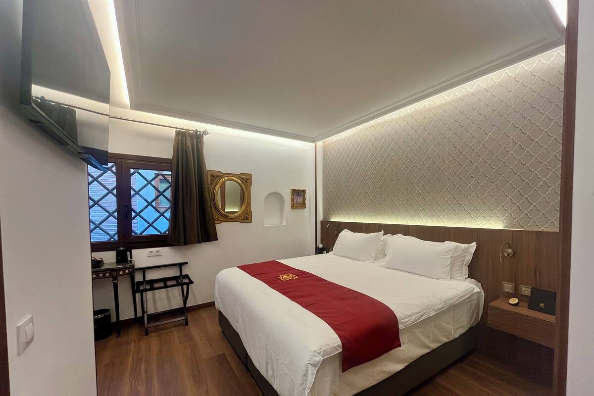 A hotel room with a large bed, a desk, a mirror, and a window with curtains.