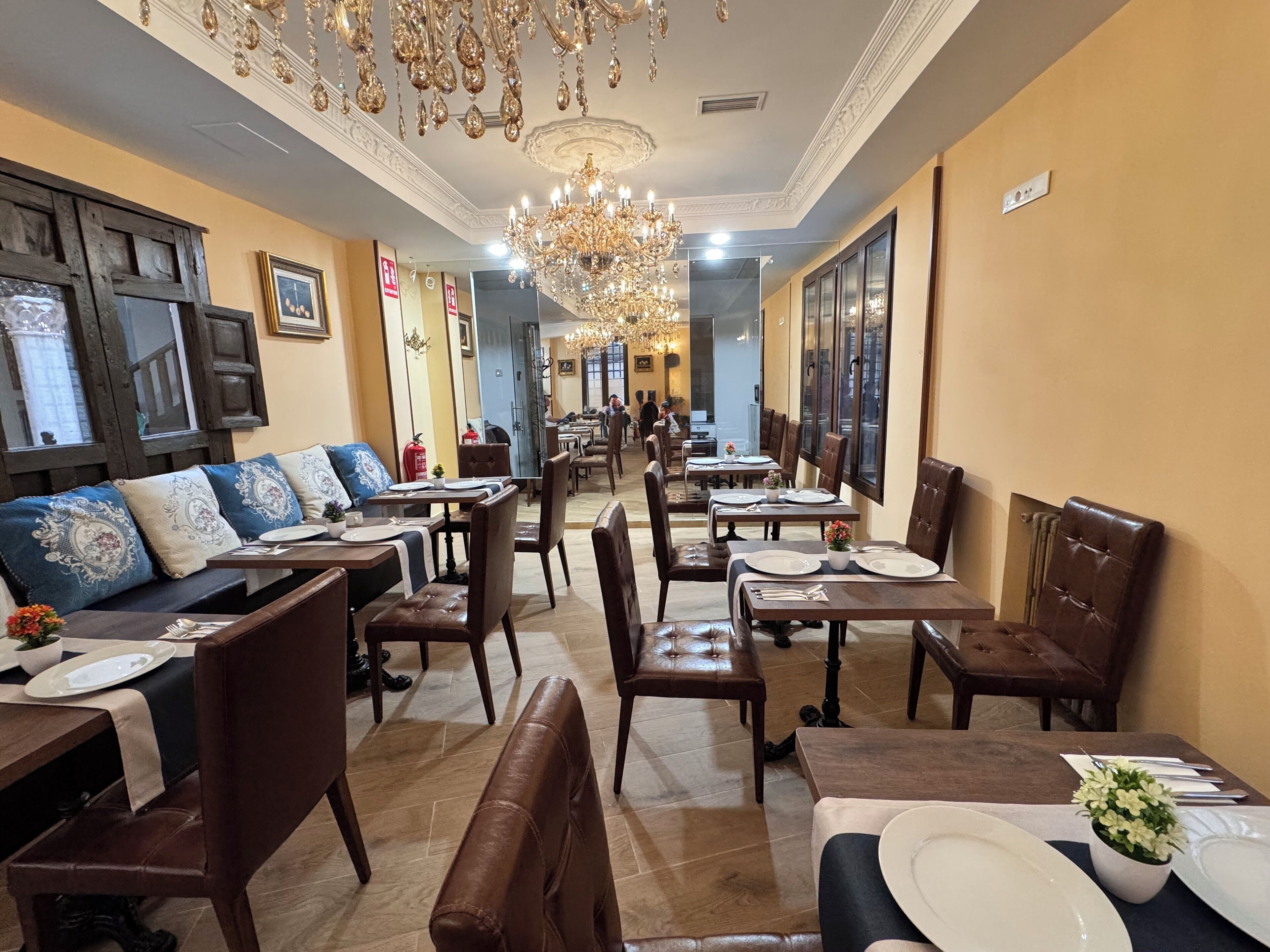 Un restaurante con una barra larga, cabinas y un candelabro. Las mesas están dispuestas con platos y cubiertos.