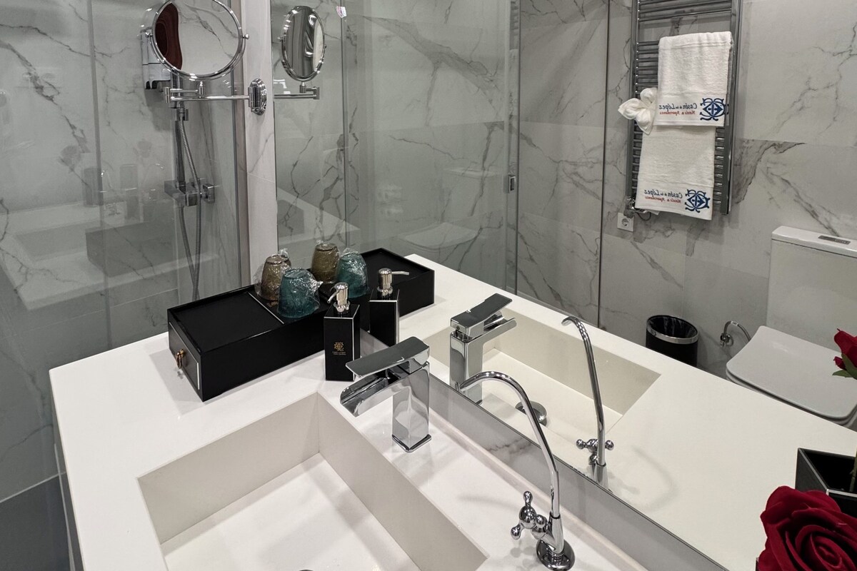 Un baño moderno con ducha de vidrio, un espejo grande y un tocador con dos lavamanos.