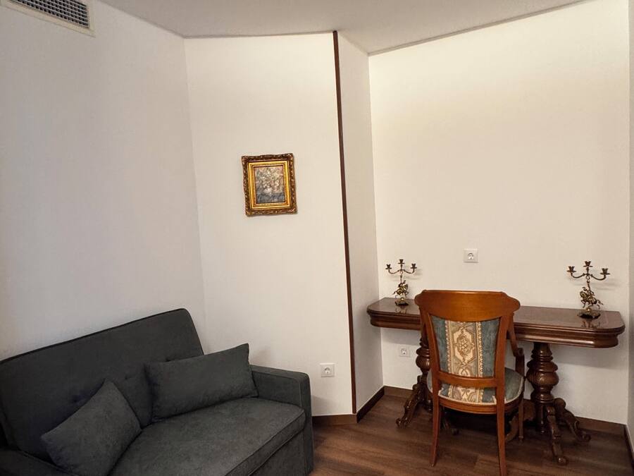 Ett rum med en grå soffa, ett matbord i trä med två stolar och en liten inramad tavla på väggen.
