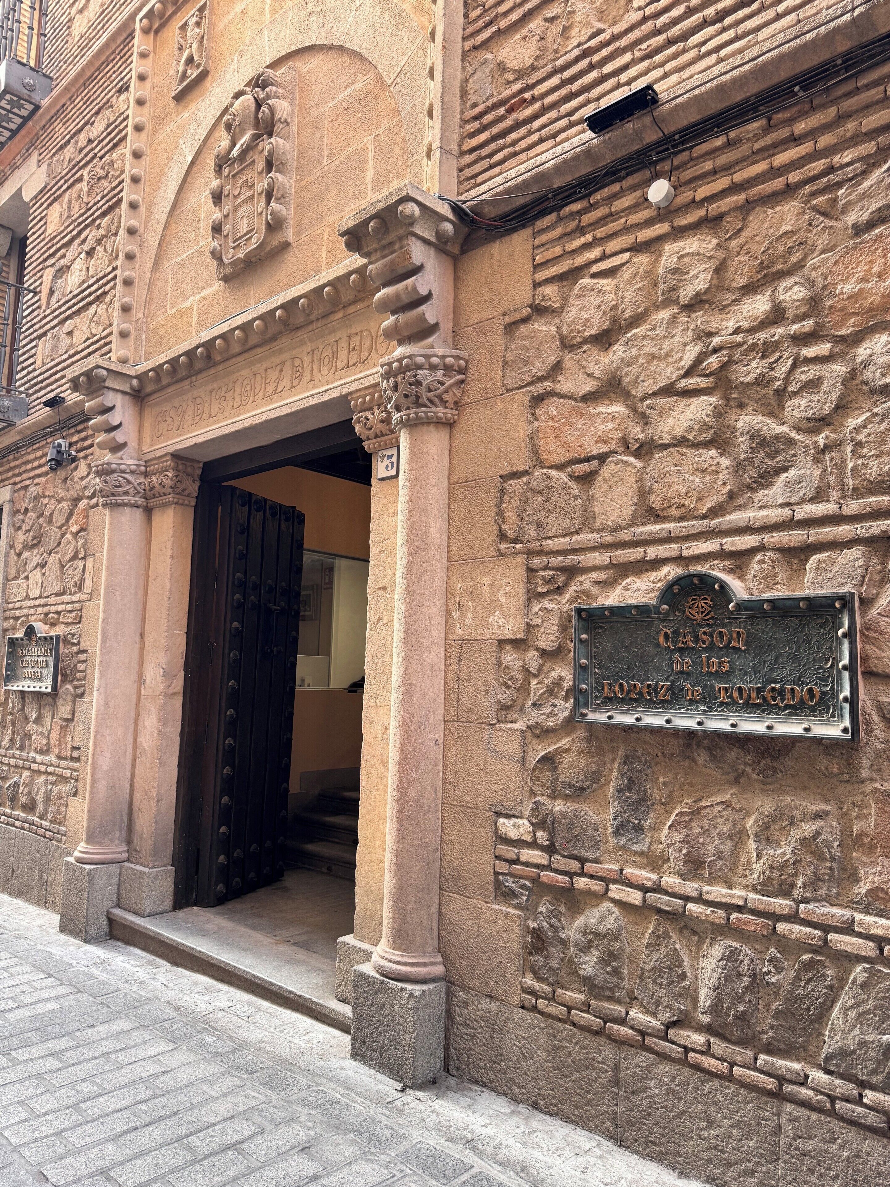Un edificio de piedra con una entrada tallada y un letrero que dice "Cason de los Lopez de Toledo".