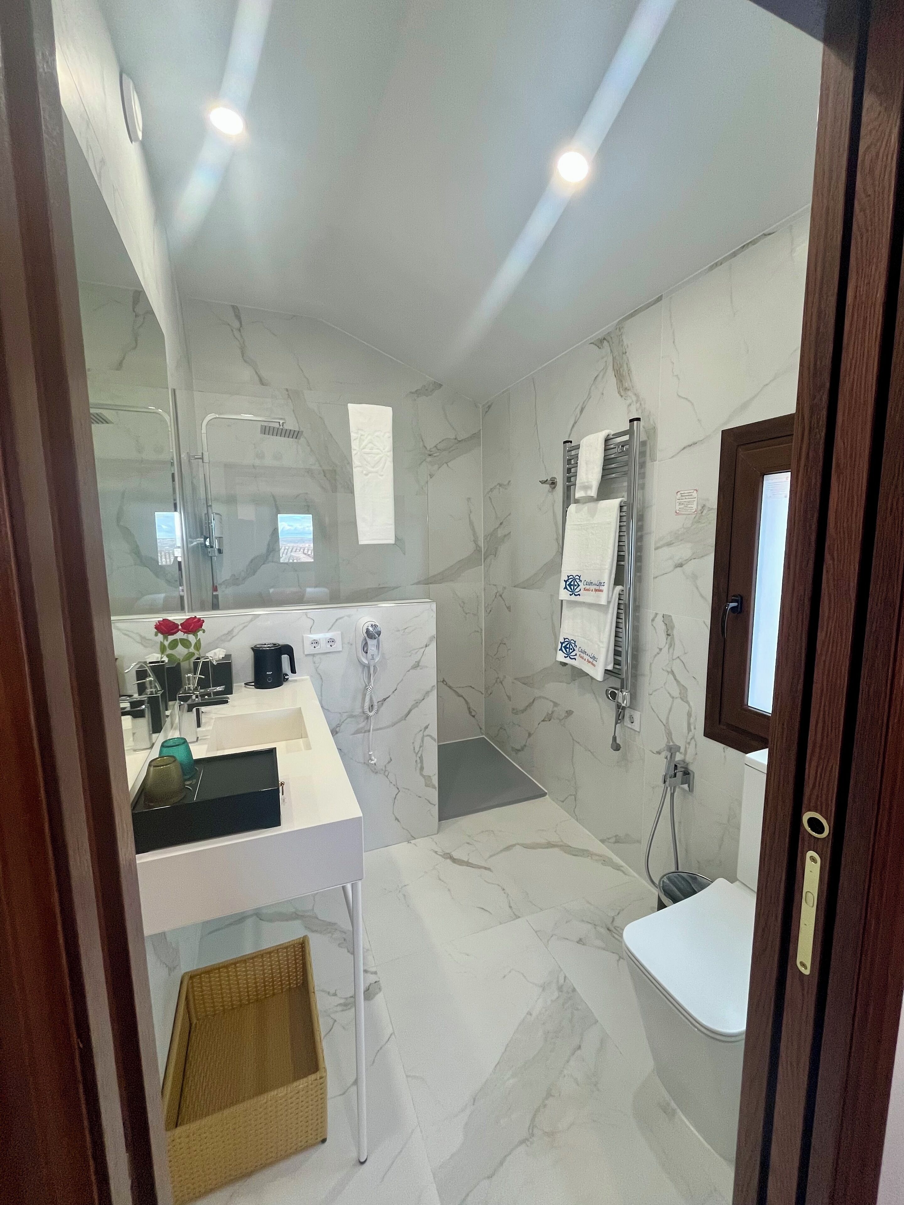 Un baño moderno con suelo de mármol, cabina de ducha de vidrio, lavabo blanco con espejo y retrete.