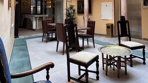 Un amplio atrio con techo alto, candelabros ornamentales y diversas disposiciones de asientos, incluyendo sillas y una mesa redonda.