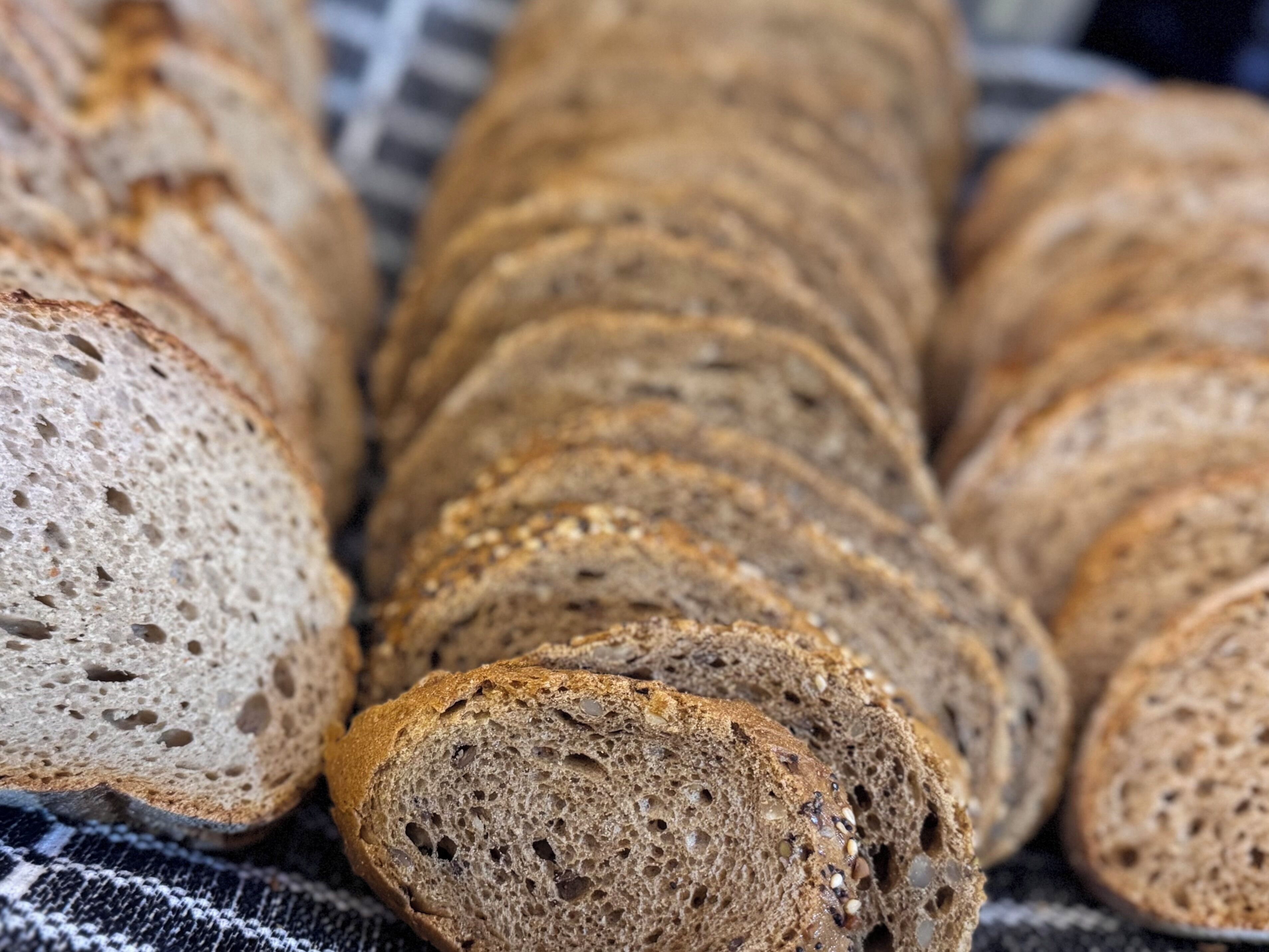 A loaf of sliced whole grain bread with visible seeds and grains, placed on a checkered cloth.