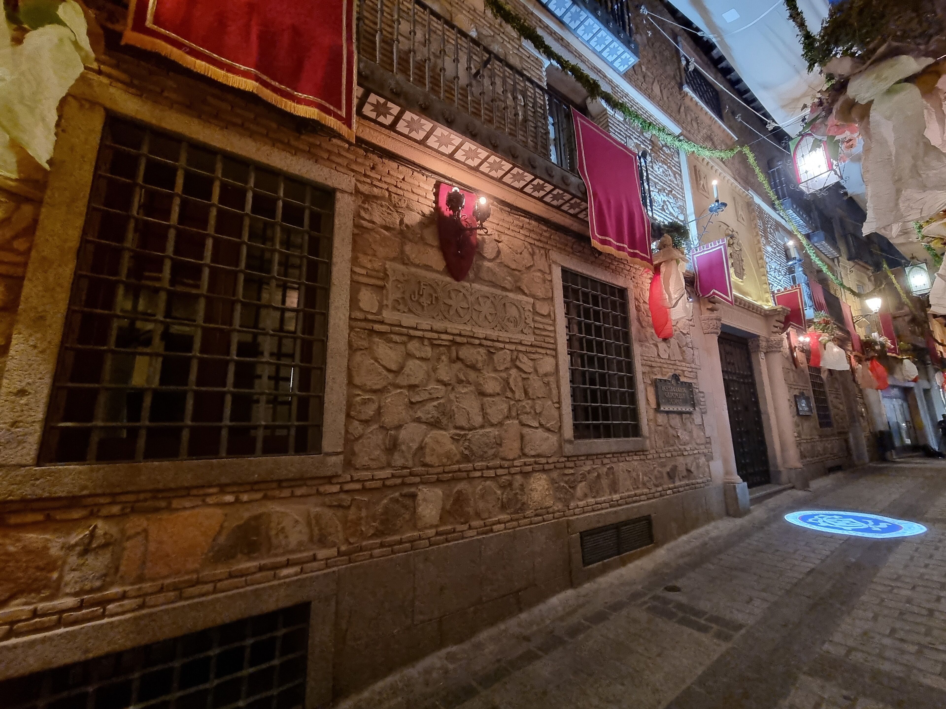 Una calle estrecha con edificios de piedra, un letrero que indica un restaurante y un símbolo circular azul en el suelo.