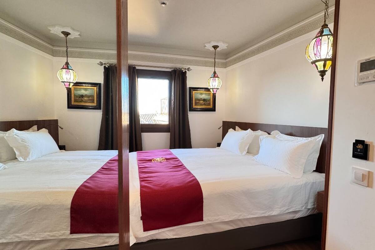 A hotel room with two beds, wooden flooring, and decorative wall sconces.