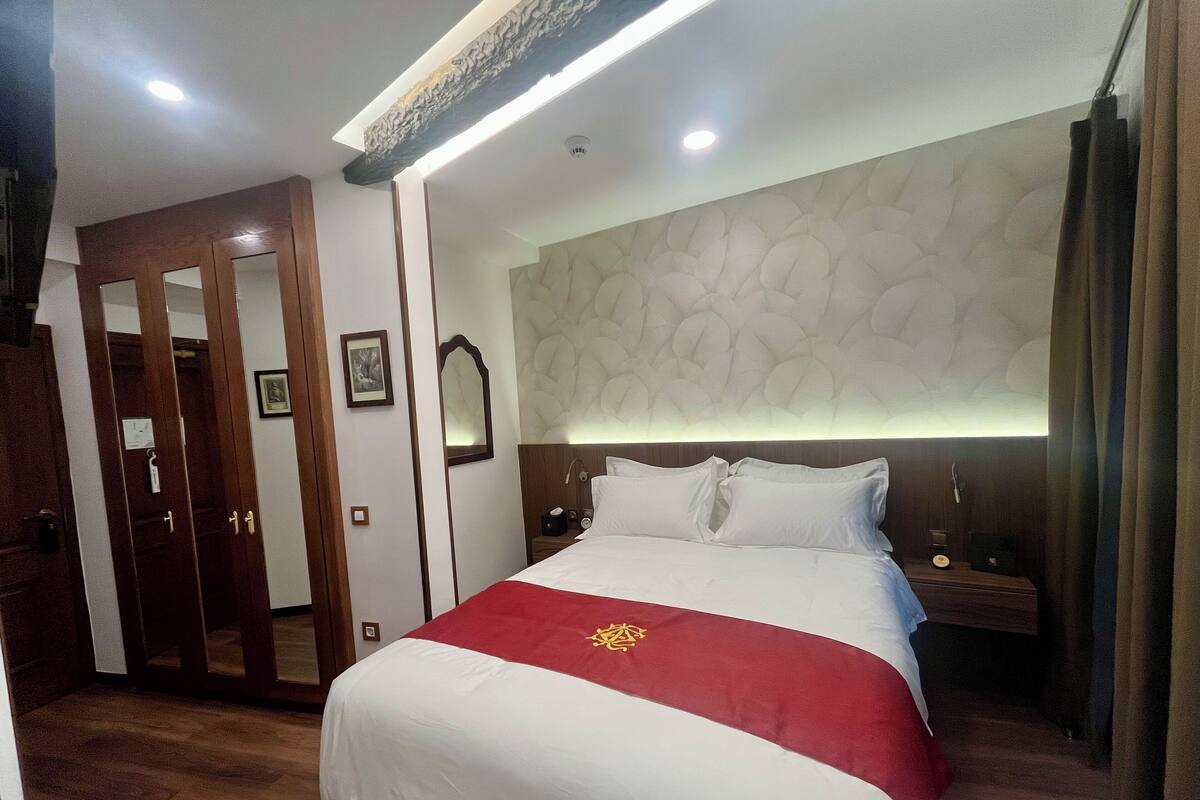 A hotel room with a large bed, wooden wardrobe, and a nightstand with a lamp.
