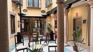 Un patio amplio con una zona de estar central, plantas en macetas y columnas de arquitectura clásica.