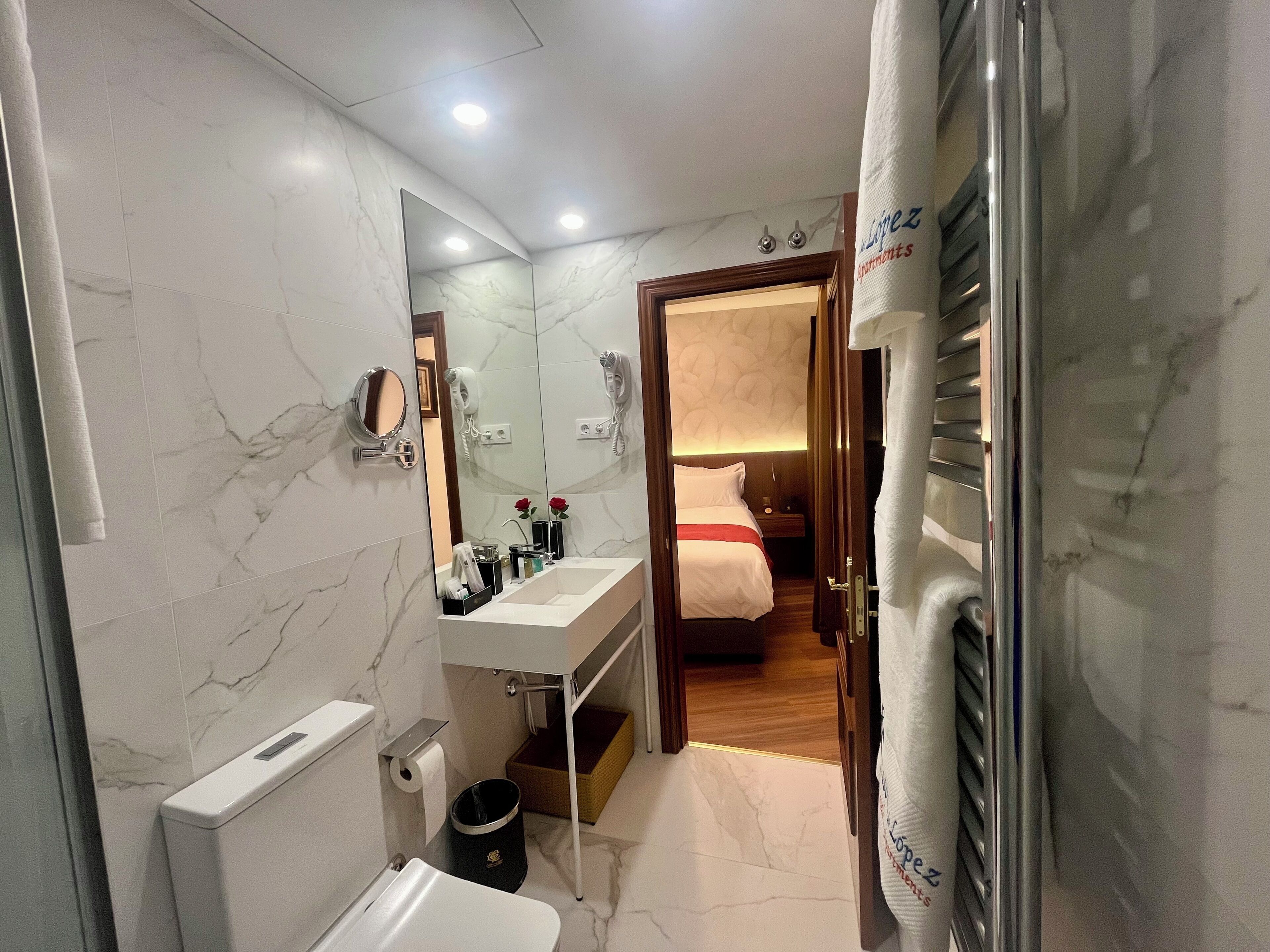 Un baño moderno con suelo de mármol, lavabo blanco, espejo y retrete.