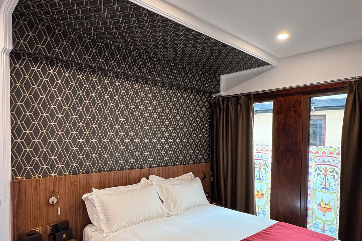 Una habitación de hotel con una cama grande, cabecera de madera y pared con un diseño geométrico.
