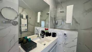 Un baño moderno con salpicadero de mármol, un espejo grande, un lavabo con bandeja negra, ducha y toallero.