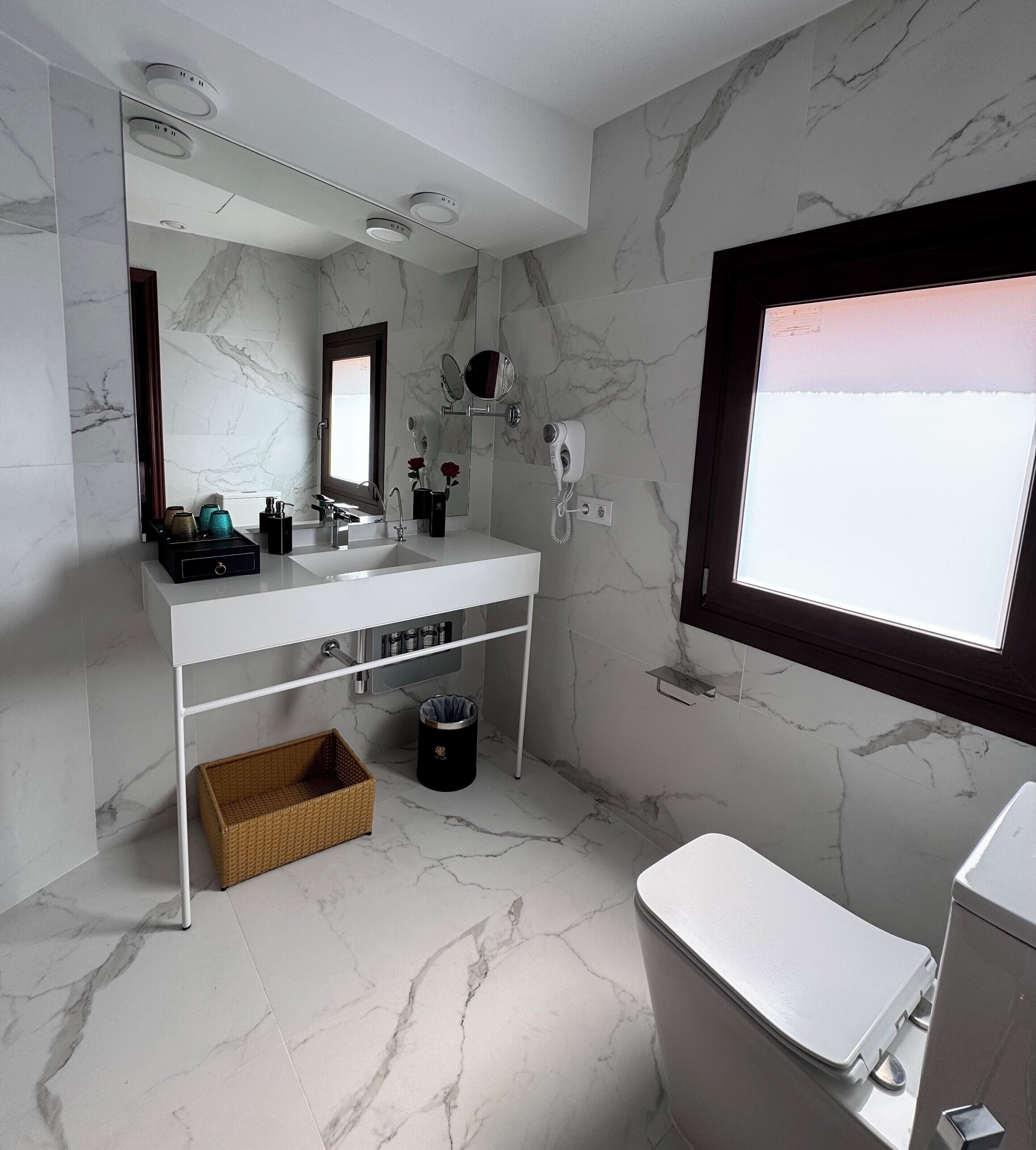 A modern bathroom with a marble backsplash, a large mirror, a vanity with a sink, and a toilet.
