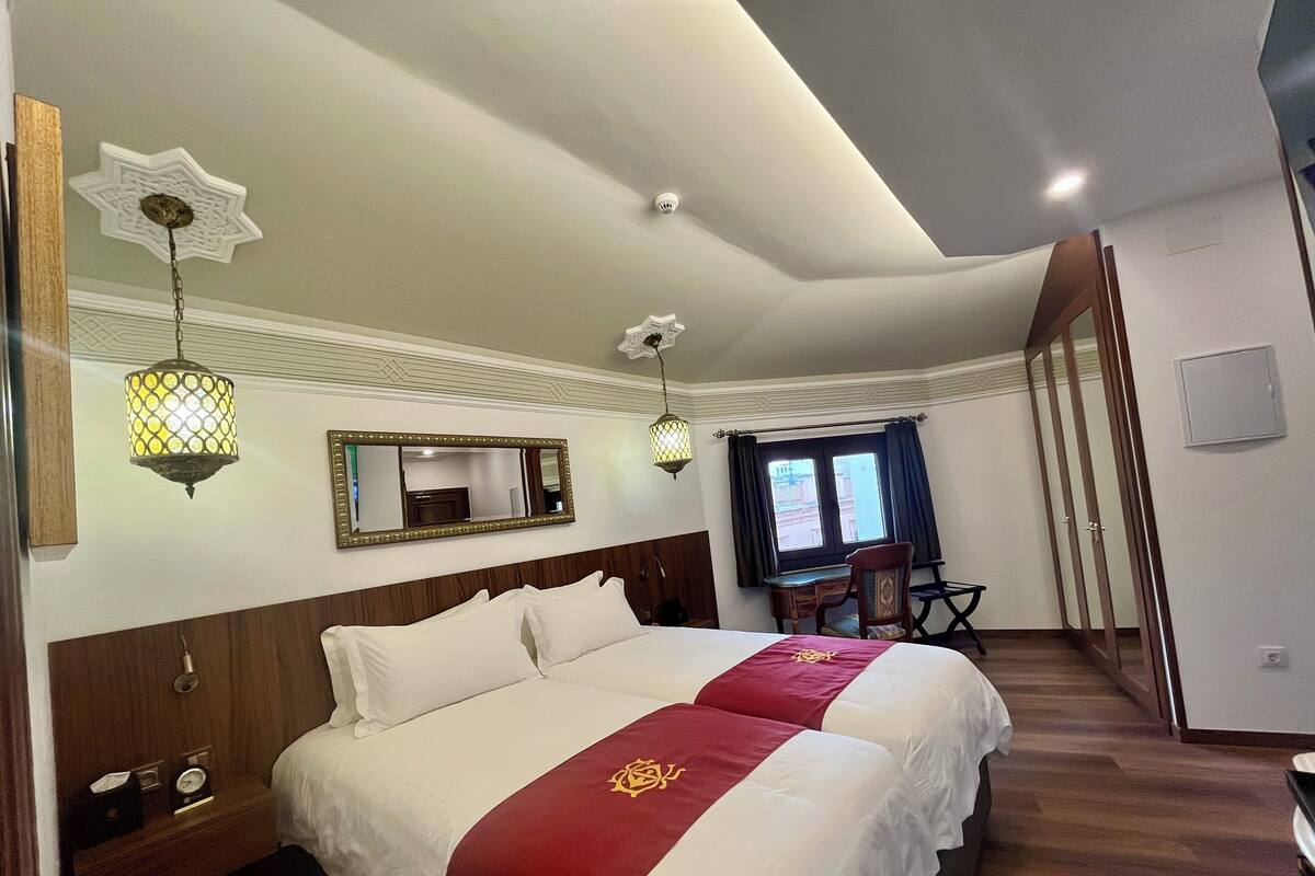 A hotel room with a large bed, a desk, a chair, a mirror, and a window with curtains.