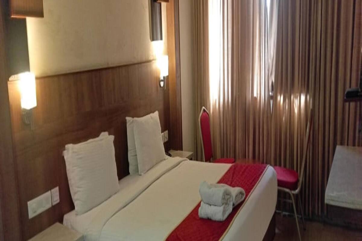 A hotel room with a large bed, a bedside table, a chair, and a desk.