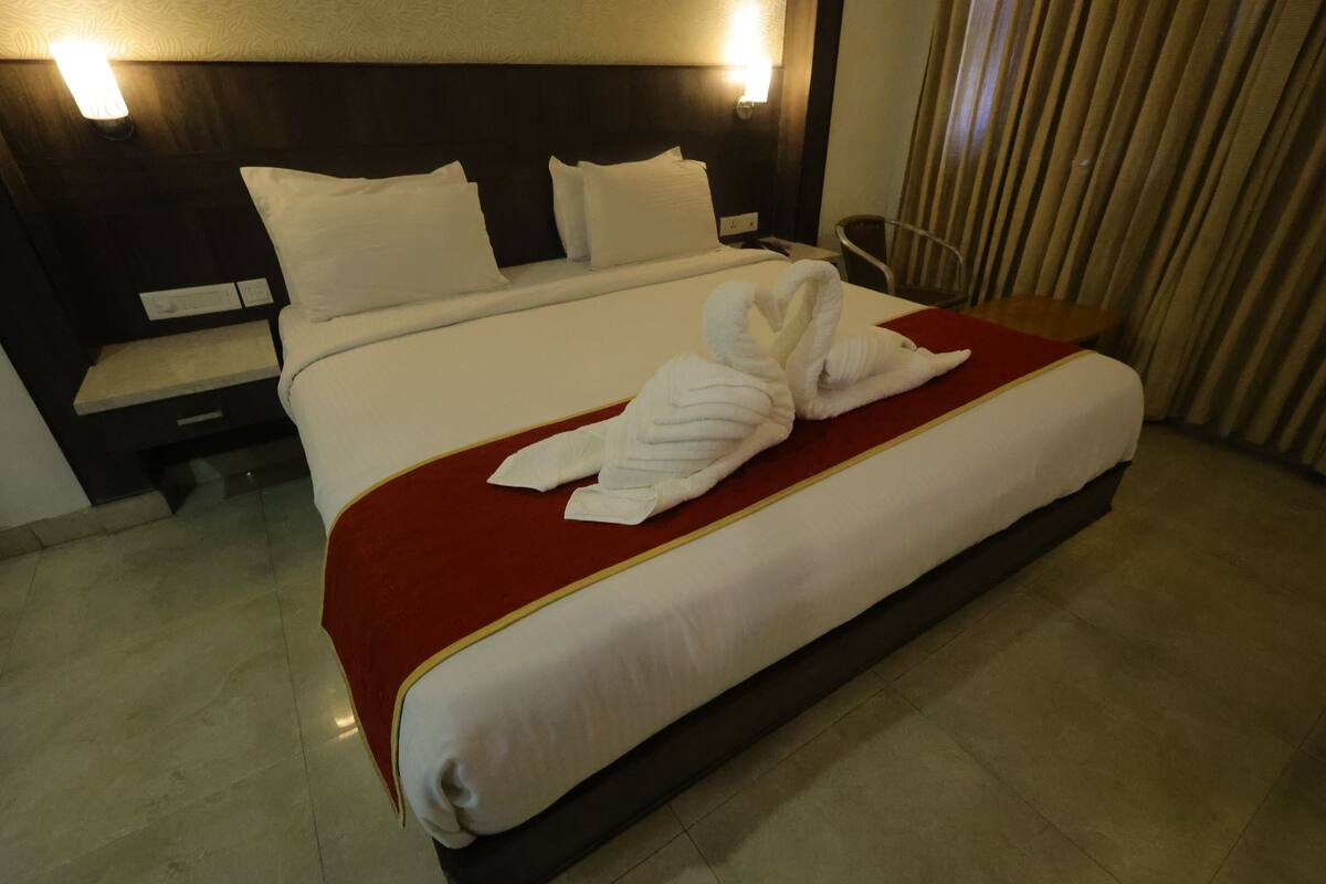 A hotel room with a large bed, a red throw blanket, and a neatly folded white towel on the bed.
