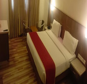 Ein Hotelzimmer mit einem großen Bett, Holzboden, Schreibtisch, Stuhl und Nachttisch.