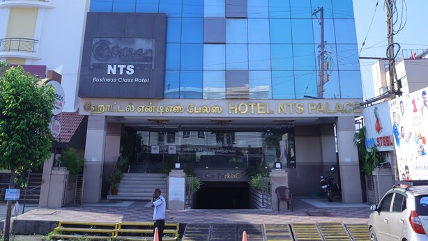 A modern hotel building with a glass facade, a sign for the NTS Business Class Hotel, and a visible entrance with steps and a parking area. - Breeze Palace (Karur)