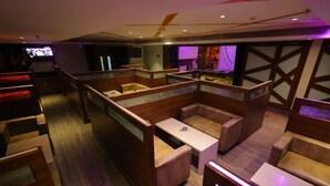 A modern bar area with wooden booths, a bar counter, and a television screen. - Breeze Palace (Karur)
