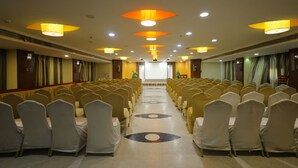 A conference room with rows of chairs, a podium at the front, and ceiling lights. - Breeze Palace (Karur)