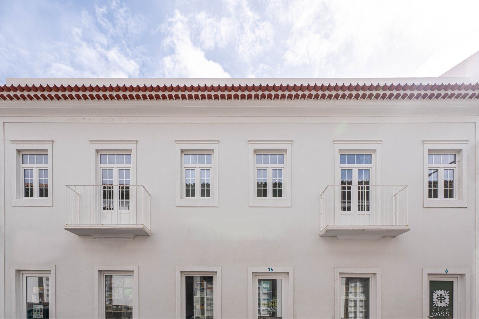 Um edifício branco com várias janelas e varandas, com telhado em azulejos e fachada plana.
