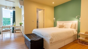 A bedroom with a bed, a desk with chairs, a bench, and a view of greenery outside. - City Oasis - Suite A (City Centre) (Ponta Delgada)