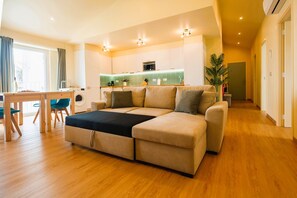 A modern living room with a sofa, a dining table with chairs, a washing machine, and a kitchen area. - City Oasis - Suite C (City Center) (Ponta Delgada)