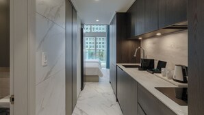 Habitación de hotel moderna con piso de mármol, una cama, kitchenette con pileta y vista a un edificio a través de un ventanal grande.