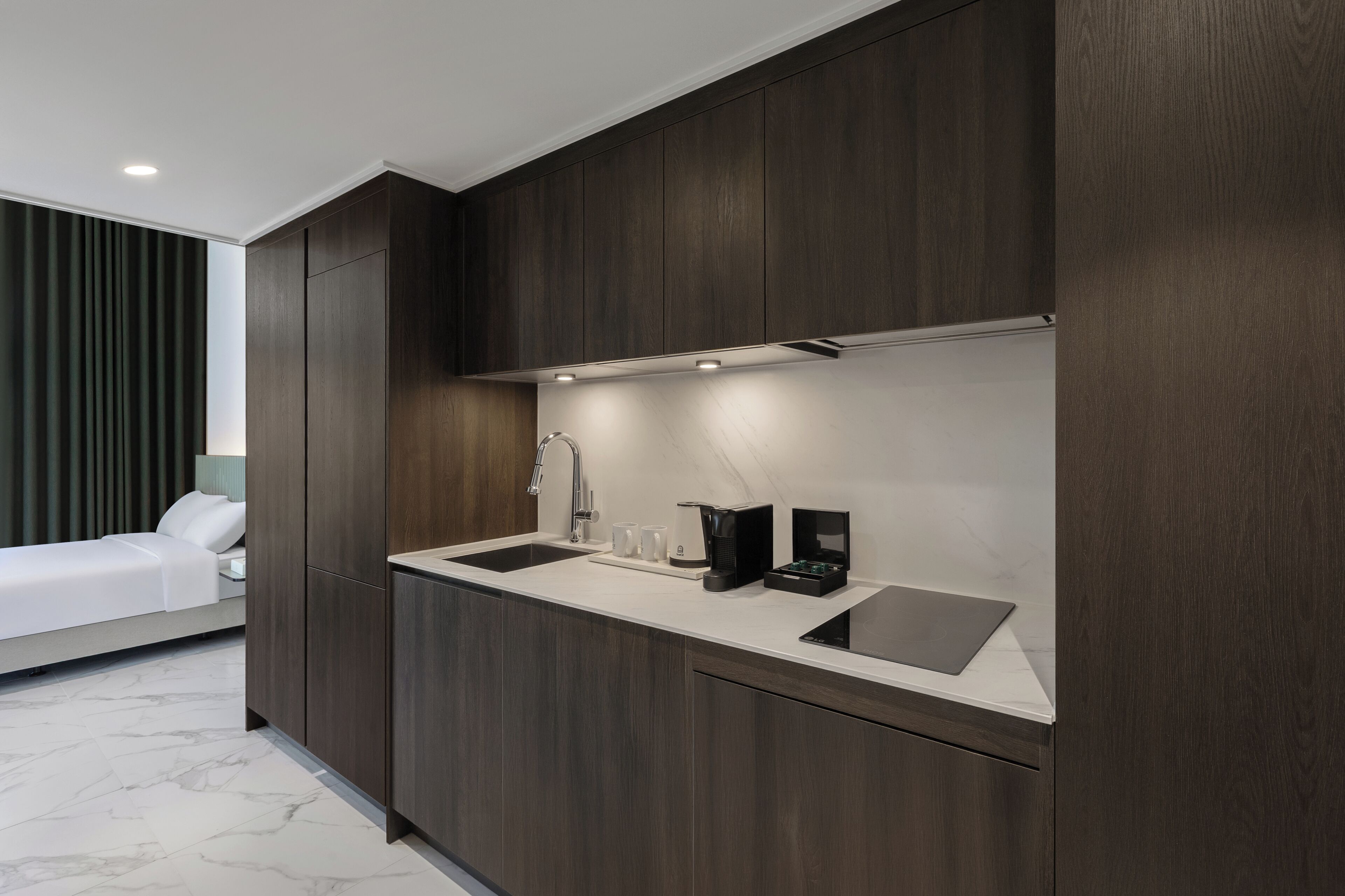 A modern kitchen with dark wood cabinetry, a countertop, a sink, and a coffee maker.