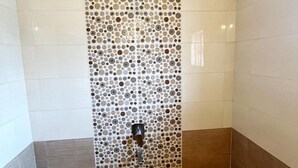 A bathroom with a tiled wall featuring a circular pattern, a showerhead, and a bucket on the floor. - Kawari Resort (Gokarna)