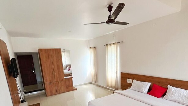 A spacious bedroom with a large bed, a wooden wardrobe, a desk, and a ceiling fan. - Kawari Resort (Gokarna)