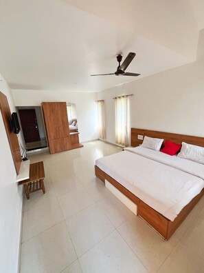 A spacious bedroom with a large bed, a wooden wardrobe, a desk, and a ceiling fan. - Kawari Resort (Gokarna)