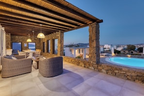 A covered outdoor seating area with stone pillars, a pool, and a view of the sea.