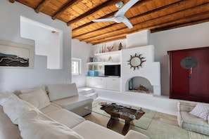 A modern living room with a wooden ceiling, white sofas, a glass coffee table, and a fireplace.