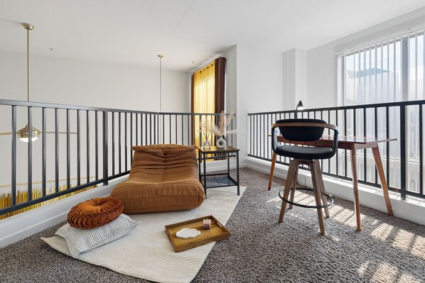 Un salón moderno con un sofá marrón, una mesita auxiliar, una silla y vistas de la ciudad a través de grandes ventanales.