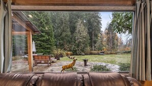 A leather sofa facing a stone patio with a deer statue, a wooden bench, and a dining table. - Sasquatch Sanctuary | New to market! (Packwood)