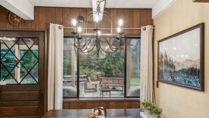 A dining area with a large table, chairs, a chandelier, and a view of an outdoor patio with a bench and table. - Sasquatch Sanctuary | New to market! (Packwood)