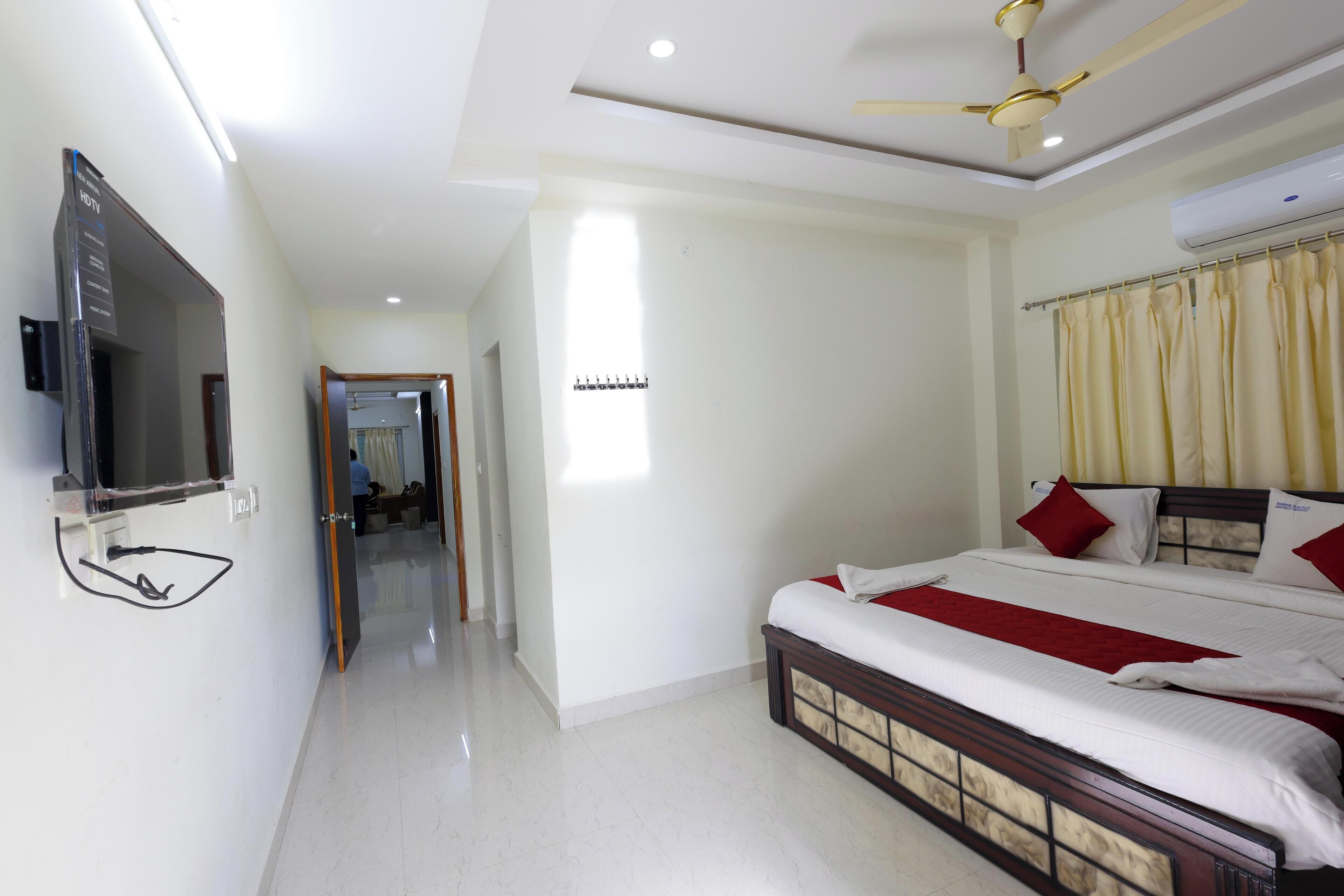 A hotel room with a bed, a TV, a ceiling fan, and a window with curtains.