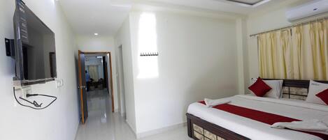 A hotel room with a bed, a TV, a ceiling fan, and a window with curtains.