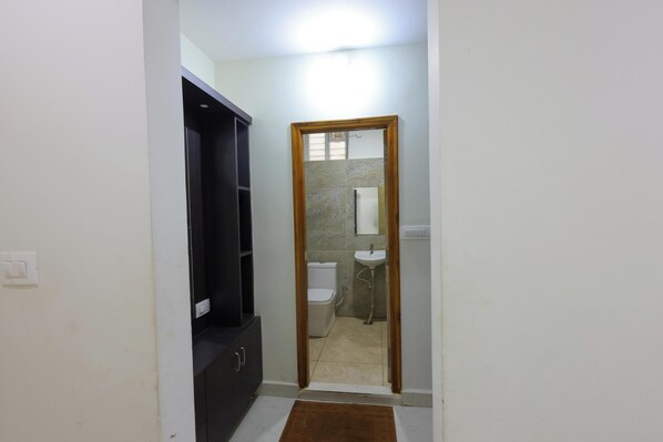 Un couloir étroit mène à une salle de bain équipée de toilettes blanches, d’un lavabo et d’un miroir.