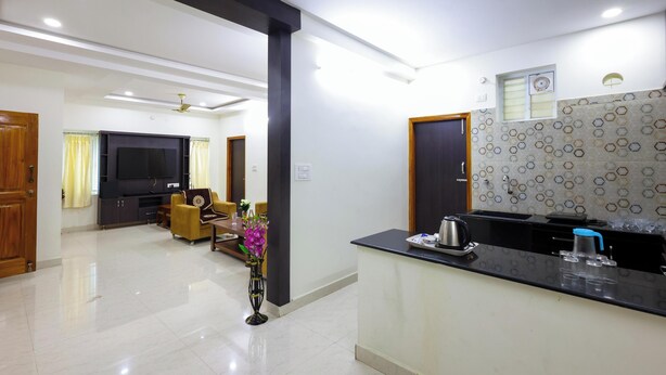A modern living room with a flat-screen TV, a sofa, and a coffee table. There is a kitchen area with a countertop and a sink. - SBHS Homestay- Venkatadri (Tirupati)
