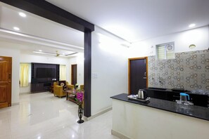 A modern living room with a flat-screen TV, a sofa, and a coffee table. There is a kitchen area with a countertop and a sink. - SBHS Homestay- Venkatadri (Tirupati)
