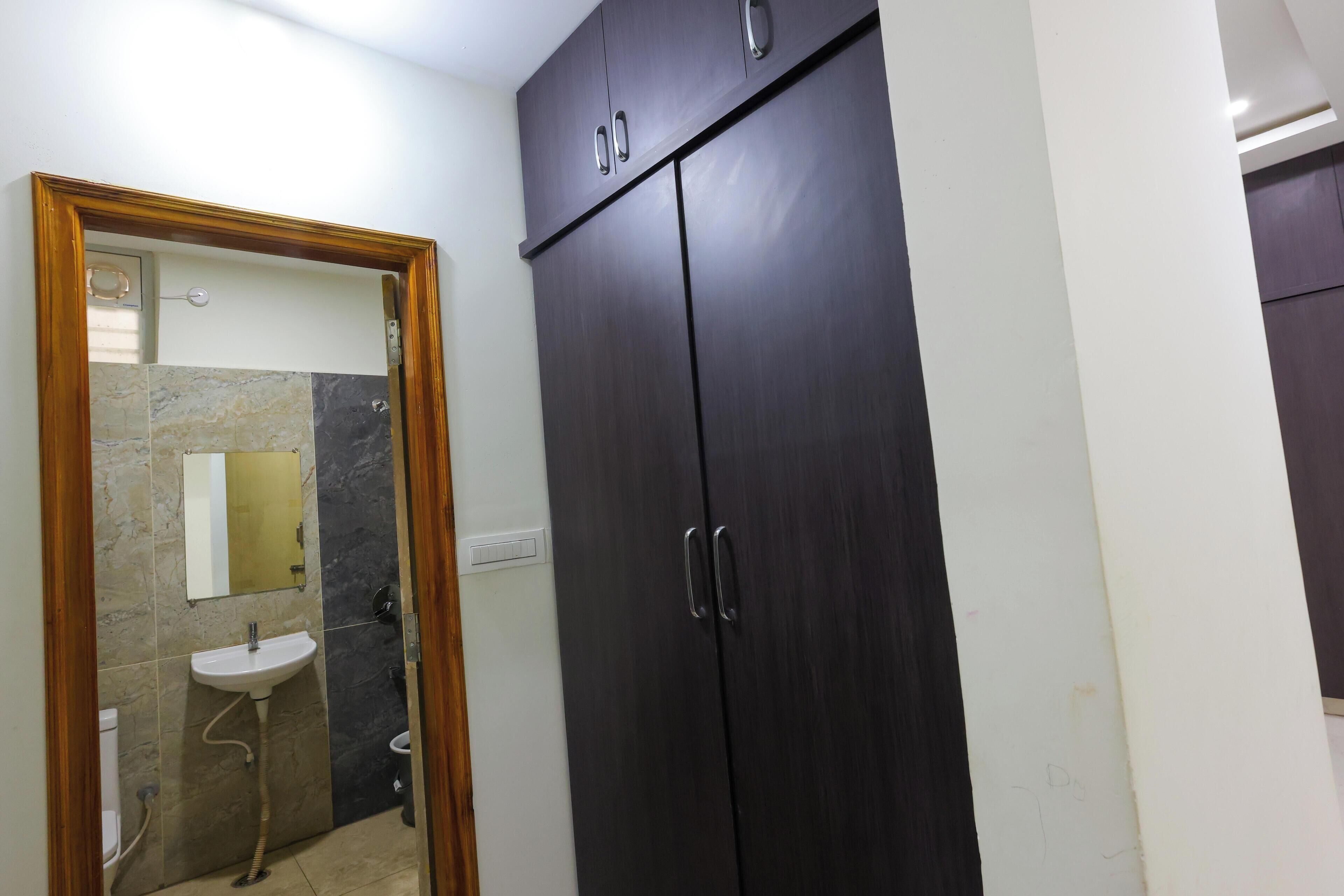 A bathroom with a dark wooden wardrobe, a white sink, and a marble-tiled wall.