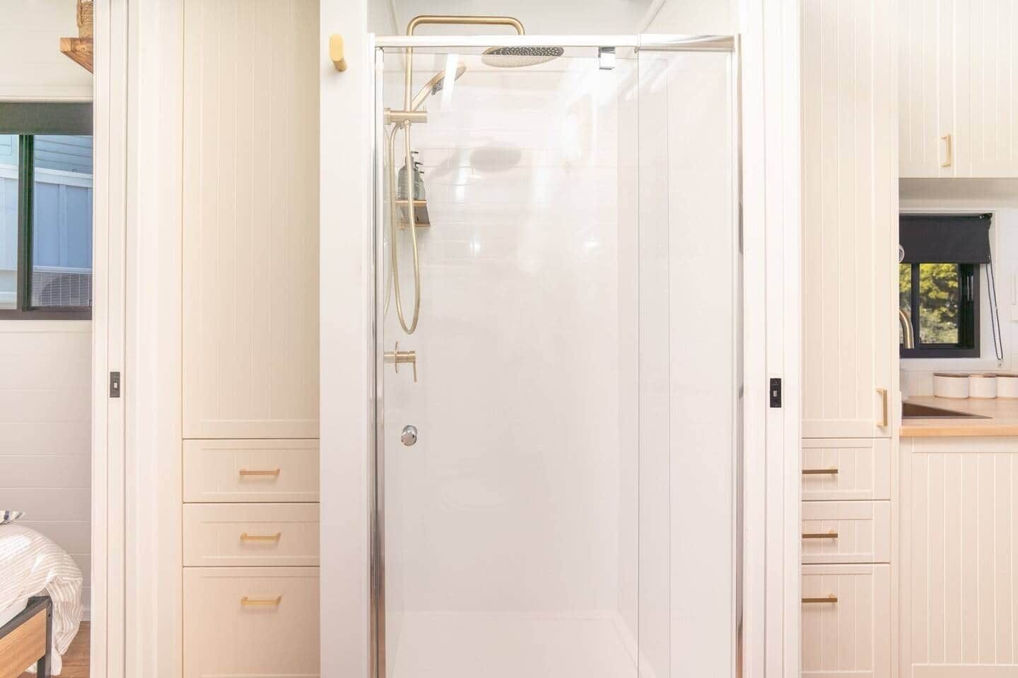 A modern bathroom with a glass shower enclosure, white cabinetry, and a small window.