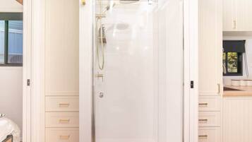 A modern bathroom with a glass shower enclosure, white cabinetry, and a small window.