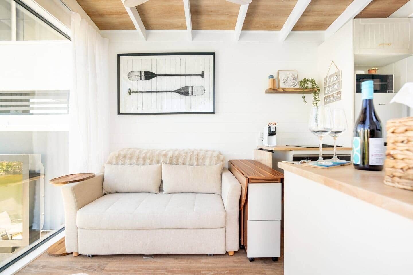 A modern living room with a sofa, a coffee table, and a kitchen area with a counter and wine glasses.