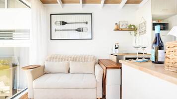 A modern living room with a sofa, a coffee table, and a kitchen area with a counter and wine glasses.